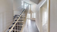 This thoughtfully designed space offers a striking first impression with its dramatic double-height entry area, where soaring ceilings draw the eye upward alongside a staircase fitted with sleek white metal balusters and dark-tread steps. The entry opens into a spacious living area finished with rich, dark hardwood-style flooring that extends throughout the main living spaces. Large windows fitted with white blinds allow generous natural light to fill the room, and a sliding glass door provides access to the exterior.

The kitchen is well-equipped with white shaker-style cabinetry extending to the ceiling, dark granite countertops, a mosaic tile backsplash in neutral tones, and a full suite of stainless steel appliances including a refrigerator, range, built-in microwave, and dishwasher.

The bedrooms are finished with plush carpeting and neutral-toned walls, creating a comfortable atmosphere. One bedroom features an ensuite bathroom with a vanity and overhead lighting. Ceiling fans are present in multiple bedrooms. Additional living or dining areas feature dark hardwood-style floors, track lighting, and multiple windows that invite natural light throughout the day.