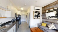 Located along E Market Street in downtown Indianapolis, this efficiently designed studio offers a thoughtful open-plan layout that maximizes every square foot. The combined kitchen and living area serves as the heart of the unit, where a galley-style kitchen lines one wall with crisp white shaker cabinetry, dark countertops, a stainless steel sink, and a full suite of black stainless appliances including a range, dishwasher, microwave, and refrigerator. Polished concrete floors run throughout, lending an urban, contemporary feel that ties the space together cohesively. The living area is anchored by a striking reclaimed wood accent wall that adds warmth and texture, complemented by a wall-mounted mini-split HVAC unit for year-round comfort. A built-in Murphy bed integrates seamlessly into the living space, providing flexible sleeping arrangements without sacrificing floor space. Large sliding glass doors flood the room with natural light and open onto a private balcony with open city views. The bathroom features a full tub-shower combination with clean white tile surround and brushed nickel fixtures. Additional conveniences include a dedicated laundry area and a closet, making this a fully functional urban residence.
