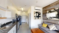 Located along E Market Street in downtown Indianapolis, this efficiently designed studio offers a thoughtful open-plan layout that maximizes every square foot. The combined kitchen and living area serves as the heart of the unit, where a galley-style kitchen lines one wall with crisp white shaker cabinetry, dark countertops, a stainless steel sink, and a full suite of black stainless appliances including a range, dishwasher, microwave, and refrigerator. Polished concrete floors run throughout, lending an urban, contemporary feel that ties the space together cohesively. The living area is anchored by a striking reclaimed wood accent wall that adds warmth and texture, complemented by a wall-mounted mini-split HVAC unit for year-round comfort. A built-in Murphy bed integrates seamlessly into the living space, providing flexible sleeping arrangements without sacrificing floor space. Large sliding glass doors flood the room with natural light and open onto a private balcony with open city views. The bathroom features a full tub-shower combination with clean white tile surround and brushed nickel fixtures. Additional conveniences include a dedicated laundry area and a closet, making this a fully functional urban residence.