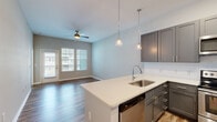 Located at 201 Sawyer Cir in Charleston, SC, this one-bedroom, one-bathroom residence offers a thoughtfully designed, single-floor layout that maximizes comfort and functionality. The open-concept kitchen and living area serves as the heart of the home, anchored by a peninsula with quartz countertops, an undermount stainless steel sink, and elegant pendant lighting overhead. The kitchen is well-appointed with gray shaker-style cabinetry, a white subway tile backsplash, and a full suite of stainless steel appliances including a range, microwave, dishwasher, and refrigerator. Wood-look plank flooring runs throughout the main living areas, lending warmth and cohesion. The living room receives natural light through large windows and a sliding glass door that opens to a balcony, complemented by a ceiling fan. The bedroom is a comfortable retreat featuring plush carpet, multiple windows with views of the outdoors, and a ceiling fan. It is served by a spacious walk-in closet outfitted with wire shelving for generous storage. The bathroom includes a gray vanity with a quartz countertop and a walk-in shower. Neutral tones and clean finishes throughout create a bright, modern ambiance well-suited to the Charleston lifestyle.