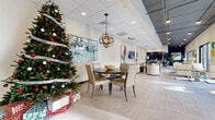 This single-floor commercial space offers a well-organized, open layout that transitions seamlessly between multiple functional zones. The entrance greets visitors with large glass doors that allow natural light to pour into the wide, tiled corridor, which is accented by decorative vases and curated artwork displayed on console tables along the walls.

The main interior unfolds into a generously sized open area finished with light-toned large-format tile flooring throughout. A central dining area features a dark round table surrounded by upholstered chairs and is anchored by a striking spherical pendant light overhead. Colorful abstract artwork adorns the crisp white walls, contributing to the modern, welcoming ambiance.

Toward one end of the space, a lounge and gathering area is distinguished by a bold navy blue accent wall housing a wall-mounted television and a beverage station. High-top tables with chrome-framed black leather chairs provide additional seating, while floor-to-ceiling windows and sliding glass doors along the perimeter deliver abundant natural light and outdoor views.

A quieter seating area with armchairs and sofas offers a more relaxed setting, while inner corridors lead to additional rooms. The dual ceiling treatment—drop tile in some areas and exposed dark industrial-style panels in others—adds architectural contrast throughout the space.