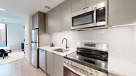 Located at 1704 N 17th St in Tampa's historic Ybor City neighborhood, this thoughtfully designed studio offers a contemporary living experience within a compact, efficiently laid-out single-floor footprint. The open-concept layout seamlessly integrates a fully equipped kitchen, living area, and sleeping space into one cohesive environment.

The kitchen is a standout feature, outfitted with stainless steel Frigidaire appliances including a refrigerator, dishwasher, electric range, and over-the-range microwave. Flat-front muted sage cabinetry extends floor to ceiling, complemented by a white quartz countertop, white subway tile backsplash, and a matte black faucet over an undermount sink — all resting on light wood-look flooring that flows throughout the space.

The living and sleeping area is bright and airy, anchored by a large floor-to-ceiling window that frames an urban view and floods the room with natural light. The space accommodates a full bed, a compact seating arrangement, and a mounted flat-screen television, creating a versatile and comfortable environment.

The bathroom features a floating vanity with a white countertop, matte black fixtures, a large mirror with integrated lighting, and a glass-enclosed walk-in shower with neutral tile surround. Clean white walls and large-format floor tiles complete the polished, modern aesthetic throughout.