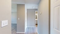 This single-floor residence offers a clean, modern interior defined by a neutral color palette of warm greige tones, light wood-style flooring, and textured ceilings throughout. The open-concept layout connects the main living area to the kitchen, which is equipped with stainless steel appliances including a range and refrigerator, crisp white cabinetry, and a peninsula countertop with a built-in sink — ideal for both cooking and casual dining. A distinctive arched doorway adds an architectural accent to the kitchen entry.

The living area is bright and airy, highlighted by sliding glass doors that open to a private balcony, framing views of lush palm trees and greenery beyond. Natural light flows generously into the space through multiple windows fitted with horizontal blinds.

The bedrooms are well-proportioned, each featuring the same warm wood-style flooring and neutral walls, with ample natural light. The bathroom is efficiently designed with a full tub-shower combination accented by white tile surround, a vanity with a light stone countertop, a framed mirror, and wood-style flooring that ties the space together cohesively. A hallway connects all areas of the unit, creating a functional and comfortable flow throughout the home.