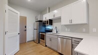 This thoughtfully designed single-floor unit at 2176 E 105th St in Cleveland, Ohio, offers a efficient and modern layout finished with contemporary materials throughout. Light-toned luxury vinyl plank flooring runs continuously across the entire space, lending warmth and visual cohesion to each area.

The kitchen serves as the functional centerpiece of the unit, featuring a full suite of stainless steel appliances, including a refrigerator, electric range, built-in microwave, and dishwasher. Cabinetry is finished in a two-tone scheme—crisp white upper cabinets paired with gray lower cabinets—each fitted with matte black hardware. A peninsula with a white quartz countertop extends into the living area, creating a natural division of space. A sliding glass door at the far end draws in natural light and provides views of the outdoors.

The bathroom is well-appointed with gray shaker-style vanity cabinetry, a white countertop, a framed sliding glass shower enclosure with bold black hardware, and a full-size mirror. A dedicated closet with built-in shelving provides practical storage. Recessed lighting and neutral gray walls maintain a clean, modern aesthetic throughout the unit.