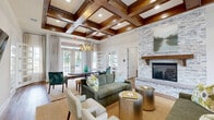 Located at 40 Cohen Walker Dr in Warner Robins, Georgia, the Encore at Beacon Place clubhouse is a thoughtfully designed single-floor community facility offering a generous array of amenity spaces. The centerpiece of the facility is a sophisticated lounge and gathering area distinguished by striking dark wood coffered ceilings, an antler-style chandelier, and a floor-to-ceiling stacked stone fireplace with a wood mantel. French doors flood the space with natural light and provide views of the surrounding greenery, while warm hardwood flooring and neutral furnishings create an inviting, upscale atmosphere. An adjacent kitchenette features granite countertops, pendant lighting, and stainless steel appliances, complementing a casual lounge area ideal for socializing. A cozy nook with a round dining table and wall-mounted TV offers an intimate setting for small gatherings or meetings. The fitness wing includes two dedicated exercise rooms — one outfitted with a full range of strength and cardio equipment on rubber flooring, and a second, light-filled studio with hardwood floors, a spin bike, and a rowing machine. A well-appointed business center provides workstations and office equipment beneath a display of the Georgia state flag, serving residents' professional needs. Throughout, the design balances rustic charm with modern comfort.