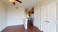 This single-floor residence is defined by rich, dark hardwood-style flooring that runs consistently throughout, creating a cohesive and polished aesthetic across all areas of the unit. The open living area is generously proportioned, with neutral-toned walls and a ceiling fan that contribute to a comfortable, airy atmosphere. Natural light filters in through blinded windows, offering views of greenery outside.

The kitchen is a well-appointed space, featuring dark espresso cabinetry that extends to the upper walls for ample storage. Granite countertops with subtle patterning complement a striking mosaic tile backsplash. Stainless steel appliances include a refrigerator, electric range, and over-the-range microwave. A white breakfast bar peninsula separates the kitchen from the living area, providing a practical transition between spaces. Track lighting above the kitchen adds focused illumination.

The bathroom continues the dark hardwood flooring and features a dark-stained vanity with a white countertop, a large mirror, and a walk-in shower enclosed by sliding glass doors. Clean white walls and crisp trim throughout the unit reinforce a modern, well-maintained character. Additional storage is accessible via a large closet with panel doors adjacent to the main living area.