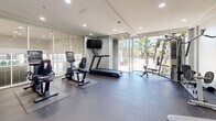 Located at 13970 Panay Way in Marina del Rey, CA, this fitness center offers a clean, modern environment designed for efficient and comfortable workouts. The space features a contemporary aesthetic with light gray walls, recessed lighting, and durable dark rubber flooring that provides both safety and ease of maintenance.

Large floor-to-ceiling windows and glass panels line one side of the room, flooding the interior with abundant natural light and offering open views of the surrounding outdoor greenery — creating an inviting atmosphere that makes workouts feel less confined. A wall-mounted flat-screen television is positioned above the cardio equipment for entertainment during exercise sessions.

The fitness center is equipped with a well-rounded selection of machines to support both cardiovascular and strength training. Cardio equipment includes treadmills and stationary bikes, while a multi-function cable strength machine and an adjustable weight bench accommodate resistance training. Full-length mirrors along one wall further enhance the sense of openness and allow users to monitor their form.

The room includes two doors, providing convenient access points, as well as a wall-mounted hand sanitizer dispenser. The overall layout is thoughtfully arranged to maximize usability within the space, making it a practical and well-appointed facility for residents in the Marina del Rey area.