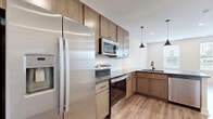 Located at 80 S. Sounders Ave in Columbus, Ohio, this single-floor unit offers a thoughtfully laid-out living space with modern finishes throughout. Light wood-tone flooring runs continuously across the entire unit, lending warmth and visual continuity to every room.

The kitchen is a standout feature, equipped with stainless steel appliances including a French door refrigerator with ice dispenser, an electric range, and an over-the-range microwave. Warm-toned shaker-style cabinetry extends to the ceiling, complemented by dark granite countertops and a white subway tile backsplash. A peninsula with a matching granite surface and an integrated sink serves as both a functional workspace and a casual dining area, illuminated by stylish pendant lights overhead.

The living room is bright and open, with multiple windows fitted with blinds that allow natural light to filter in while providing views of the surrounding neighborhood. Recessed lighting adds to the clean, modern aesthetic.

The combined bathroom and laundry area is efficiently designed, featuring granite countertops, dark-finished cabinetry, and a stacked washer and dryer unit. An adjacent walk-in closet offers generous wire shelving for organized storage. A utility room rounds out the layout, ensuring practical functionality throughout this well-appointed Columbus residence.