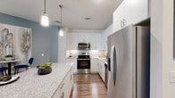 This single-floor residence showcases a contemporary open-concept design that seamlessly connects the kitchen, dining, and living areas. The living room is highlighted by a signature slate-blue accent wall, wood-style flooring, a ceiling fan, and a set of French doors that invite natural light and provide outdoor access. A compact dining nook adjacent to the living area offers additional functionality within the shared space.

The kitchen is well-equipped with stainless steel appliances, including a range, microwave, dishwasher, and a large side-by-side refrigerator. Crisp white cabinetry extends to the ceiling for ample storage, complemented by a white subway tile backsplash, granite countertops, and pendant lighting over a generous island that doubles as a breakfast bar.

The bedrooms offer a calm, restful atmosphere with neutral tones, wood-style flooring, ceiling fans, and multiple windows providing generous natural light. The bathroom features a granite-topped vanity, white cabinetry, wood-style flooring, and a tub-shower combination. Consistent finishes throughout — including granite surfaces and hardwood-style floors — create a cohesive and polished aesthetic across the entire residence.
