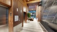 This elegant building lobby is a study in modern design, blending warm materials with contemporary architecture to create a welcoming and functional amenity floor. The entry corridor immediately impresses with its rich vertical wood slat paneling, terrazzo tile flooring, and a dramatic dark feature wall etched with an intricate city map graphic, lending an artistic and urban character to the space.

The corridor opens into a generously proportioned lounge area anchored by a full-wall built-in shelving unit crafted in warm wood tones, complete with integrated accent lighting and a large flat-screen display. Plush, earth-toned seating arrangements — including a modular sectional sofa, accent chairs, and organic-shaped coffee tables — create an inviting gathering space beneath soaring ceilings and a statement drum pendant light. Lush potted plants throughout add a natural, refreshing element to the interior.

Adjacent to the lounge, a well-equipped fitness center features modern cardio machines, including a treadmill and elliptical, with floor-to-ceiling glass doors that open directly to a private outdoor courtyard. The courtyard offers an intimate al fresco setting with a dining table, garden seating, lush greenery, and overhead string lights that lend a warm, convivial ambiance. Elevators with sleek finishes provide convenient vertical access throughout the building.