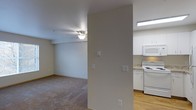 This single-floor residential unit offers a clean, functional layout designed for comfortable everyday living. The living area is finished with wall-to-wall carpeting and features a ceiling fan with integrated lighting, lending a practical and cozy ambiance to the space. Neutral-toned walls throughout create a bright, cohesive feel that easily accommodates a variety of furnishing styles. A structural column partially divides the living area from the kitchen, maintaining an open sense of flow between the two spaces. The kitchen is equipped with white appliances, including a freestanding range, over-the-range microwave, and refrigerator, all complemented by white cabinetry and light-toned countertops. The kitchen flooring transitions to hardwood-style material, providing a clean contrast to the carpeted living space. Recessed fluorescent lighting illuminates the kitchen area efficiently. Multiple wall switches are conveniently positioned throughout, and the overall layout reflects a straightforward, well-maintained design. The space is well-suited for those seeking a tidy, move-in ready environment with a simple and practical aesthetic.