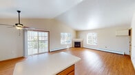This single-floor residence offers a thoughtfully designed open-concept layout that seamlessly connects the kitchen, dining, and living areas. The living room is a standout space, featuring soaring vaulted ceilings that amplify the sense of openness, warm hardwood flooring, and a corner fireplace framed in light stonework. Multiple windows and sliding glass doors flood the area with natural light and provide views of the outdoors. Baseboard heating runs throughout, ensuring consistent comfort year-round.

The kitchen is well-appointed with rich medium-toned wood cabinetry, white appliances including a range, microwave, refrigerator, and dishwasher, and a central island with a light countertop that serves as both a prep space and a natural divider from the living area. Tile flooring grounds the kitchen zone.

A hallway connects the private areas of the home, including bedrooms finished with hardwood flooring and ceiling fans, as well as a bathroom featuring a vanity with warm wood cabinetry and a wide countertop. Warm neutral tones, wood trim detailing, and consistent flooring choices throughout the home create a cohesive and inviting atmosphere from room to room.