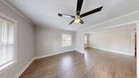 Located at 214 Emanuel Cleaver II Blvd in Kansas City, Missouri, this single-story, 2-bedroom, 1-bathroom unit offers a practical and comfortable layout finished with consistent, neutral-toned interiors throughout. Dark hardwood-style flooring runs continuously across the living areas and bedrooms, providing a cohesive aesthetic that complements the soft gray walls and bright white trim and baseboards.

The living area is generously proportioned, featuring crown molding, a textured ceiling, and a ceiling fan with integrated lighting. A wide archway connects the living space to an adjoining room, creating an open, connected feel and allowing natural light to pass through multiple windows fitted with horizontal blinds.

The bedrooms are well-sized, each offering natural light through windows with street-facing views of the surrounding neighborhood. One bedroom includes a closet with a wooden hanging rod, while both rooms maintain the same neutral palette and hardwood-style flooring.

The kitchen is equipped with white cabinetry, granite-look countertops, a stainless steel gas range, dishwasher, and a single-basin sink — offering a clean and functional cooking space with light-toned flooring distinct from the rest of the unit.