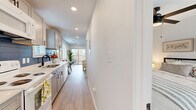 This efficiently designed single-floor residence offers a thoughtfully organized layout comprising a living room, bedroom, kitchen, bathroom, and hallway. Light wood-tone flooring flows consistently throughout, creating a cohesive and airy aesthetic across all rooms.

The galley-style kitchen is a standout feature, equipped with gray shaker cabinetry, quartz countertops, a stainless steel sink with a matte black faucet, and a striking blue subway tile backsplash. Recessed lighting illuminates the workspace, and a plantation-shuttered window adds natural light.

The living room is bright and open, benefiting from a sliding glass door that connects to an outdoor patio area. A ceiling fan with integrated lighting provides both comfort and function, while clean white walls offer a neutral backdrop.

The bedroom is a calm and restful space, featuring a ceiling fan, a double-door closet, and a window with blinds that allows for natural light. The bathroom is well-appointed with a dual-sink white vanity topped with a quartz surface, matte black fixtures, and a large mirror, complemented by light wood flooring that continues from the main living areas.

Overall, the space presents a clean, modern aesthetic with consistent finishes throughout.