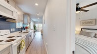 This efficiently designed single-floor residence offers a thoughtfully organized layout comprising a living room, bedroom, kitchen, bathroom, and hallway. Light wood-tone flooring flows consistently throughout, creating a cohesive and airy aesthetic across all rooms.

The galley-style kitchen is a standout feature, equipped with gray shaker cabinetry, quartz countertops, a stainless steel sink with a matte black faucet, and a striking blue subway tile backsplash. Recessed lighting illuminates the workspace, and a plantation-shuttered window adds natural light.

The living room is bright and open, benefiting from a sliding glass door that connects to an outdoor patio area. A ceiling fan with integrated lighting provides both comfort and function, while clean white walls offer a neutral backdrop.

The bedroom is a calm and restful space, featuring a ceiling fan, a double-door closet, and a window with blinds that allows for natural light. The bathroom is well-appointed with a dual-sink white vanity topped with a quartz surface, matte black fixtures, and a large mirror, complemented by light wood flooring that continues from the main living areas.

Overall, the space presents a clean, modern aesthetic with consistent finishes throughout.