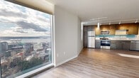 Located at 809 S Washington St in Seattle's First Hill neighborhood, this 610-square-foot, one-bedroom, one-bathroom unit delivers a modern high-rise living experience with striking urban and waterfront views. The open-concept living area and kitchen are anchored by expansive floor-to-ceiling windows that frame panoramic views of Puget Sound, the Seattle port, and the downtown skyline, flooding the space with natural light. Light wood-tone laminate flooring runs throughout the living areas, complemented by an exposed concrete structural column that adds an industrial design element to the otherwise clean, contemporary aesthetic.

The kitchen features a galley-style layout with flat-front dark wood upper cabinetry, gray lower cabinets, a light blue glass tile backsplash, and a full suite of stainless steel appliances, including a refrigerator, electric range, microwave, and dishwasher. Track lighting overhead enhances functionality. The bedroom, measuring 100 square feet, is finished with plush carpet, tall windows with city views, and a sliding-door closet with built-in shelving. The bathroom includes wood-toned cabinetry, granite countertops, and wood-look vinyl flooring. Throughout, neutral tones and clean lines create a cohesive, contemporary atmosphere.