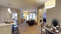 This well-appointed two-bedroom, two-bathroom residence is designed with an open-concept layout that promotes a seamless flow between living areas. The living room features plush carpeting, a door providing access to the outdoors, and large windows that allow natural light to fill the space. A defined dining area sits near the entry, finished with wood-style flooring and pendant lighting overhead.

The kitchen is equipped with rich dark cabinetry extending to the ceiling, stainless steel appliances including a gas range, built-in microwave, and refrigerator, complemented by light countertops and a central island with a sink and bar seating. Track lighting and pendant fixtures illuminate the workspace, and an in-unit washer and dryer are conveniently accessible nearby.

Both bedrooms are generously proportioned with soft carpet, ceiling fans, and ample natural light. The primary bedroom includes a walk-in closet and an en-suite bathroom featuring dark cabinetry, a wide vanity with a large mirror, and wood-style flooring. The second bathroom offers a full tub-shower combination. Neutral wall tones and consistent finishes throughout contribute to a cohesive, comfortable ambiance.