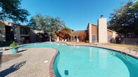 Located at 6425 Bankside Dr in Houston, Texas, this residential community offers a welcoming outdoor environment defined by classic brick architecture and lush, mature tree coverage. The buildings feature a combination of light-toned brick and warm wood-toned siding, lending a timeless aesthetic to the community's exterior. Staircases and private balconies with metal railings are visible along the building facades, providing residents with outdoor access and elevated views of the grounds.

At the heart of the community is a generously sized, freeform outdoor swimming pool with clear turquoise water, framed by a textured concrete and brick pool deck. Lounge chairs are positioned along the deck, creating a comfortable area for relaxation under the open Texas sky. A prominent brick chimney and a screened structure adjacent to the pool area add to the architectural character of the community.

Mature oak and deciduous trees are scattered throughout the grounds, providing natural shade across the pool area and walkways. Iron fencing defines and secures various sections of the property, contributing to both the aesthetic and safety of the community. Wall-mounted lighting fixtures on the brick exteriors ensure well-lit pathways. The overall ambiance is one of a comfortable, established residential community designed for outdoor enjoyment.