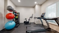 This fitness center at 307 E 1st St in Dayton, Ohio, offers a practical and well-organized space designed to support a comprehensive workout routine. The room features durable rubber-speckled flooring throughout, providing a safe and resilient surface suitable for a variety of exercise activities. Neutral-toned walls and recessed lighting create a clean, functional environment, while windows fitted with blinds allow natural light to filter in, contributing to an open and airy atmosphere.

The cardio section is equipped with True-brand treadmills and an elliptical trainer, each outfitted with digital consoles for tracking workout metrics. A stationary cycling bike with an integrated tablet display rounds out the cardio offerings. On the strength and functional training side, the space includes a well-stocked rack holding an assortment of dumbbells in varying weights, alongside a collection of medicine balls and stability balls in multiple sizes, accommodating a range of fitness levels and training styles.

Access to the fitness center is provided through a sturdy metal door, and wall-mounted utility panels are positioned conveniently near the entrance. The overall layout is efficiently organized, maximizing the usable floor area while keeping equipment accessible and the space uncluttered.