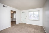 This single-floor unit offers a straightforward and functional layout designed for comfortable everyday living. The living area is generously proportioned, featuring warm beige carpeting, white walls, and a textured ceiling. Large windows allow natural light to fill the space, and an open passageway connects the living area to an adjoining room, which also features a ceiling fan and its own window — ideal for use as a dining area or additional sitting room. A front entry door provides direct access to the living space.

The kitchen is equipped with white cabinetry extending to the ceiling, dark laminate countertops, and white appliances including a refrigerator, electric range, and an overhead range hood. The flooring transitions to durable tile, and under-cabinet lighting adds functional illumination to the workspace.

The bathroom features matching tile flooring, a white vanity with dark countertop, a large wall mirror with overhead lighting, and a tub-shower combination. Grab bars are present for added accessibility.

The bedrooms are carpeted and finished in neutral tones, each with at least one window offering outdoor views and ample wall space for furniture arrangement. The overall ambiance of the unit is clean, bright, and move-in ready.