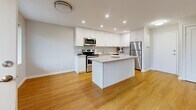 This 2-bedroom, 1-bathroom single-floor residence offers a clean, modern aesthetic with a practical and efficient layout. Warm hardwood-style flooring runs consistently throughout every room, creating a cohesive and inviting atmosphere.

The kitchen is a standout feature, outfitted with crisp white shaker cabinetry extending to the ceiling, stone-look countertops, a subway tile backsplash, and a full suite of stainless steel appliances including a range, built-in microwave, and refrigerator. A central island provides additional prep space and opens to the adjacent living area, which benefits from large windows that invite natural light and offer views of the surrounding neighborhood.

Both bedrooms are well-proportioned and feature double-door closets, neutral wall tones, and windows that bring in natural light. The primary bedroom is notably spacious, offering generous built-in closet storage. The second bedroom also includes a closet and a bright window overlooking a green outdoor view.

The bathroom is finished with a granite-topped white vanity, an undermount sink, and a chrome fixture, reflecting the same clean and contemporary style found throughout the unit. Additional storage is provided by a dedicated closet. The overall ambiance is bright, neutral, and move-in ready.