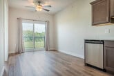 Located at 4185 Timothy Ct in De Forest, Wisconsin, this single-floor unit offers a thoughtfully designed layout that maximizes every square foot. The open kitchen serves as the heart of the space, featuring rich dark-stained cabinetry, light countertops, and a full suite of stainless steel appliances including a range, microwave, dishwasher, and refrigerator. Light wood-tone flooring runs throughout the main living and kitchen areas, adding warmth and continuity to the design. Recessed lighting overhead keeps the kitchen bright and functional.

The spacious primary bedroom is finished with plush carpet, a ceiling fan with light fixture, and a generously sized closet with bifold doors and built-in shelving. A large window frames scenic outdoor views of the surrounding greenery, filling the room with natural light. A baseboard heating unit ensures year-round comfort.

A dedicated laundry room provides added convenience, housing a stacked washer and dryer unit alongside additional shelving. The entryway features a bold dark-paneled door that makes a clean, modern statement against the crisp white walls. Overall, the space presents a clean, contemporary aesthetic with practical finishes suited for everyday living.