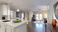 This well-appointed single-floor residence combines modern design with functional living across a thoughtfully arranged open floor plan. The kitchen serves as a centerpiece, showcasing white shaker cabinetry, quartz countertops, stainless steel appliances including a refrigerator, range, and microwave, and a large island with an undermount sink and seating for multiple bar stools. Elegant pendant lighting illuminates the workspace, while wood-look flooring flows seamlessly throughout the main living areas. The open layout connects the kitchen directly to the dining area and living room, creating an ideal space for entertaining. The living room is bright and inviting, featuring vaulted ceilings, a ceiling fan, and French doors that invite natural light and provide outdoor access. The bedroom is a serene retreat, complete with plush carpet, a ceiling fan, natural light from large windows, and ample space for a king-sized bed and dresser. The bathroom features large-format neutral tile surrounding a soaking tub with chrome fixtures, delivering a clean and polished aesthetic. A dedicated in-unit laundry closet with a full-size washer and dryer adds everyday convenience. Throughout the residence, a neutral color palette and contemporary finishes create a cohesive, modern ambiance.