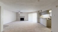 This single-floor unit offers a practical and comfortable layout across a compact but efficiently utilized footprint. The open-concept living room and kitchen serve as the heart of the space, with plush wall-to-wall carpeting throughout the living area providing a warm, inviting atmosphere. A standout feature of the living room is the classic fireplace framed by a built-in shelving unit, ideal for display or storage. A ceiling fan overhead adds to the comfort of the space, while a sliding glass door dressed with vertical blinds fills the room with natural light and provides access to the outdoors. The kitchen is equipped with gray cabinetry, granite-style countertops, a breakfast bar peninsula, a black refrigerator, a dishwasher, and light wood-style flooring, creating a clean and functional cooking space. A dedicated walk-in closet offers generous shelving and hanging storage. The bathroom features light wood-style tile flooring, a vanity with cabinet storage, and a shower-tub combination with a safety grab bar. The textured ceilings and neutral color palette throughout lend the space a cohesive, understated aesthetic well-suited for a variety of décor styles.