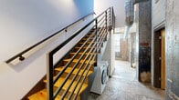 Located at 144 4th St in Burlington, NC, this two-floor industrial loft seamlessly merges historic character with contemporary design. The main floor commands an impressive footprint, featuring a striking blend of exposed brick walls, polished and raw concrete floors, and white-painted brick that floods the space with a sense of industrial authenticity. Large grid-pane windows allow abundant natural light to pour into the open living areas, highlighting the raw textures and generous ceiling height throughout.

The kitchen is outfitted with rich dark cabinetry, granite countertops, and stainless steel appliances, set against an exposed brick backdrop with a large window that brightens the workspace. Two bathrooms offer clean, modern finishes including dark wood vanities and granite counters. The upper level houses the spacious primary bedroom, which benefits from natural light and a warm hardwood floor, complemented by an exposed brick accent wall and a substantial concrete architectural element that speaks to the building's storied past.

A standout open-riser staircase with a sleek black metal railing connects the two floors, with a washer and dryer cleverly tucked underneath. The dedicated laundry area on the upper level provides additional convenience. Two closets and a hallway round out the practical layout of this distinctive urban loft.