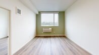 Located at 311 Capitol Way N in downtown Olympia, Washington, this single-floor unit offers a clean, modern design with light wood-style flooring throughout. The open-concept kitchen is a standout feature, boasting white shaker cabinetry, gray countertops, a large peninsula island, stainless steel appliances including a refrigerator, range, and dishwasher, and stylish pendant lighting that adds warmth to the space. Ample upper and lower cabinet storage makes this kitchen as functional as it is attractive. The living and bedroom areas are bright and well-proportioned, with large windows that invite natural light and offer pleasant views of the surrounding Olympia cityscape and greenery. The bedrooms feature light-toned walls, generous closet space with sliding doors and built-in rods, and individual climate control units. The bathroom is finished in a consistent modern palette, featuring a white vanity with gray countertops, clean white walls, and wood-style flooring. A dedicated laundry area with an in-unit washer is also present. Throughout the space, the design emphasizes simplicity, functionality, and a bright, airy ambiance.