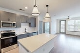 Located at 2501 Gunbarrel Rd in Chattanooga, TN, this well-designed 2-bedroom, 3-bathroom single-floor residence offers a thoughtful layout with modern finishes throughout. The open-concept kitchen and living area serves as the heart of the home, showcasing grey flat-panel cabinetry, a striking white quartz island with pendant lighting overhead, a geometric tile backsplash, and a full suite of stainless steel appliances. Light wood-look flooring runs through the main living areas, creating a clean, contemporary feel. The living room is bright and open, with natural light flowing in through large windows and a glass door that leads to an outdoor area. The primary bedroom is a comfortable, well-proportioned space featuring a ceiling fan, wood-look flooring, and access to a walk-in closet with built-in wire shelving. The second bedroom offers plush carpet flooring, a ceiling fan, and a window with outdoor views. Three bathrooms provide ample convenience for residents and guests alike. A dedicated laundry room and three closets add significant storage and functionality to the unit. The overall design is clean, bright, and modern, with a neutral color palette that enhances the sense of openness throughout the space.