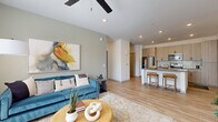 Located in Buckeye, Arizona, this two-bedroom, two-bathroom residence offers a thoughtfully designed single-floor layout with modern finishes throughout. The open-concept living area is bright and welcoming, featuring light wood-style flooring, recessed lighting, and a ceiling fan. Large windows dressed with linen curtains and blinds allow generous natural light to fill the space, creating an airy atmosphere.

The kitchen is well-appointed with light wood cabinetry, stainless steel appliances including a refrigerator, range, and microwave, complemented by a white subway tile backsplash and gray quartz countertops. A central island with bar seating provides a casual dining option and connects seamlessly to the living area.

The primary bedroom features a calming blue accent wall, a ceiling fan, and a window with outdoor views, lending a serene retreat feel. The second bedroom mirrors this comfortable aesthetic. Both bathrooms showcase light wood vanity cabinetry with gray countertops and wood-look tile flooring; one bathroom includes a walk-in glass-enclosed shower, while the other offers a clean, functional layout.

Two hallways connect the space efficiently, and the consistent use of neutral tones and modern hardware throughout creates a cohesive, contemporary ambiance ideal for everyday living.