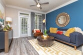 This thoughtfully designed single-floor residence offers a cohesive blend of modern style and functional living. The kitchen is outfitted with warm honey-toned cabinetry, granite countertops, stainless steel appliances including a range and built-in microwave, a tile backsplash, and a double-basin sink set into a peninsula that opens toward the dining area. Crown molding and track lighting add a polished finish to the space.

The living area makes a strong visual statement with a deep teal accent wall adorned with large-scale equestrian artwork, flanked by floor lamps. Rich hardwood flooring, crown molding, and a ceiling fan contribute to the room's warmth and character. A dining nook sits adjacent, bathed in natural light.

The bedroom continues the teal accent wall theme, featuring a decorative arrangement of circular mirrors above the upholstered headboard. A ceiling fan, sheer-curtained windows, and a built-in shelving workspace nook make it both restful and functional.

The bathroom is finished with granite countertops, warm wood vanity cabinetry, a large framed mirror with globe lighting, tile flooring, and a shower-tub combination enclosed by a curtain with white tile surround. Every room reflects a consistent, well-curated design aesthetic throughout.