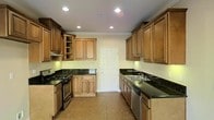 This two-story home offers a functional and refined layout designed for comfortable living. The kitchen stands out as a central highlight, showcasing warm honey-toned raised-panel wood cabinetry that extends to the ceiling, providing generous storage throughout. Dark green granite countertops add a bold contrast against the cabinetry, while recessed lighting illuminates the space with a bright, clean ambiance. The kitchen is equipped with stainless steel appliances, including a gas range and dishwasher, making it well-suited for everyday cooking and entertaining. Crown molding details along the ceiling lend a classic, polished character to the space. Neutral tile flooring runs throughout the kitchen, offering both durability and a timeless aesthetic. A paneled door at the far end of the kitchen provides additional access, contributing to the home's practical flow. The two-floor layout of the home allows for a natural separation between living and private spaces, a hallmark of traditional home design. Overall, the space combines classic architectural detailing with functional features, creating an inviting and well-structured environment throughout both levels.