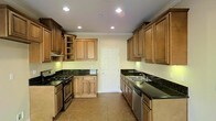 This two-story home offers a functional and refined layout designed for comfortable living. The kitchen stands out as a central highlight, showcasing warm honey-toned raised-panel wood cabinetry that extends to the ceiling, providing generous storage throughout. Dark green granite countertops add a bold contrast against the cabinetry, while recessed lighting illuminates the space with a bright, clean ambiance. The kitchen is equipped with stainless steel appliances, including a gas range and dishwasher, making it well-suited for everyday cooking and entertaining. Crown molding details along the ceiling lend a classic, polished character to the space. Neutral tile flooring runs throughout the kitchen, offering both durability and a timeless aesthetic. A paneled door at the far end of the kitchen provides additional access, contributing to the home's practical flow. The two-floor layout of the home allows for a natural separation between living and private spaces, a hallmark of traditional home design. Overall, the space combines classic architectural detailing with functional features, creating an inviting and well-structured environment throughout both levels.