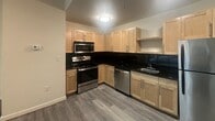 Located in Richmond, Virginia's historic Church Hill neighborhood, Unit 302 at 420 N 18th St is a thoughtfully designed studio-style residence that blends modern finishes with industrial character. The space occupies a single floor and makes efficient use of its layout throughout.

The kitchen is a standout feature, offering light maple cabinetry paired with striking black countertops and a coordinating backsplash. Stainless steel appliances — including a refrigerator, range, microwave, and dishwasher — provide a fully functional cooking space that feels polished and contemporary.

The main living area is defined by two contrasting design elements: a dramatic exposed brick wall that adds warmth and historic texture, and a large floor-to-ceiling glass window wall that floods the room with natural light and frames views of the surrounding Richmond streetscape. Framed glass interior sliding doors with gold-toned frames provide a stylish separation between spaces while maintaining an open, airy feel.

Durable gray wood-look flooring runs throughout, tying the distinct areas together cohesively. A closet offers practical storage, and the bathroom completes the unit's functional amenities. The overall ambiance balances the character of a historic building with clean, updated interiors suited for modern urban living.
