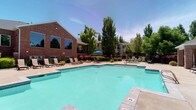 This residential community presents an inviting outdoor environment centered around a generously sized swimming pool with clear, turquoise water. The pool area is thoughtfully designed with a wide concrete deck that accommodates multiple lounge chairs, providing ample space for relaxation and recreation. A shaded seating area with a blue umbrella and patio furniture offers a comfortable spot for gathering and socializing.

The surrounding architecture features classic red brick construction with large windows that allow for abundant natural light. Multi-story residential buildings frame the pool area, creating a sense of enclosure and community while maintaining an open, airy atmosphere. Mature trees and well-maintained landscaping, including flowering shrubs and manicured greenery, provide natural shade and add vibrant color to the outdoor setting.

The overall ambiance is one of a well-maintained, resort-style community where outdoor living is a central focus. The combination of the sparkling pool, thoughtfully arranged seating, and lush greenery creates a welcoming and relaxing environment. The single-floor layout of the featured space integrates seamlessly with the outdoor amenities, making it an ideal setting for those who value both comfort and community living.