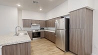 Located at 13404 N 30th Ave in Phoenix, AZ, this single-story home offers five bedrooms, three bathrooms, and four closets within a thoughtfully designed floor plan. The open-concept kitchen and living area serves as the heart of the home, featuring a large center island with a granite countertop and integrated sink, complemented by matching granite surfaces along the perimeter. Warm wood-grain cabinetry with brushed metal hardware lines the walls, and a full suite of stainless steel appliances—including a refrigerator, range, and microwave—provides a modern, functional cooking space. Recessed lighting illuminates the kitchen, which flows seamlessly into an open living area with clean white walls and light wood-look flooring that extends throughout the home. Each of the five bedrooms is bright and well-proportioned, featuring the same wood-look flooring, white panel doors, and vertical-blind windows that allow natural light to fill the space. The three bathrooms are finished consistently with wood-grain vanities, granite countertops, and combination tub/shower units with sliding glass enclosures. One bathroom is equipped with grab bars, offering added accessibility. Four closets provide ample storage throughout the home.