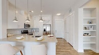 Located at 3350 W Friendly Ave in Greensboro, NC, this single-story residence offers a clean, modern aesthetic defined by bright white walls, warm wood-look flooring, and thoughtfully selected finishes throughout. The open-concept kitchen is a standout feature, showcasing crisp white cabinetry, a subtle blue-gray tile backsplash, stainless steel appliances including a French door refrigerator and electric range, and a generous island with quartz countertops and seating for two. Pendant lighting with brushed nickel fixtures adds a polished touch overhead. The kitchen flows naturally into the living area, which is bathed in natural light from large French doors that offer views to the outdoors. The living space features elevated ceilings with a ceiling fan, creating a bright and airy atmosphere. A built-in shelving nook provides both functional storage and display space. The bedroom is carpeted for comfort and includes a ceiling fan, natural light from a window with blinds, and a serene neutral color palette. The bathroom is well-finished with subway tile in the tub/shower surround, wood-look tile flooring, white cabinetry, and quartz countertops. Throughout the residence, the cohesive design language of neutral tones and modern fixtures creates a welcoming, move-in-ready environment.