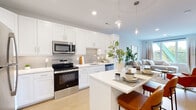 This well-appointed 2-bedroom, 3-bathroom single-story residence offers a thoughtfully designed open-concept layout with clean, modern finishes throughout. The kitchen serves as a central hub of the home, featuring crisp white shaker cabinetry, a tiled backsplash, stainless steel appliances including a range, microwave, and dishwasher, and a white quartz-topped island with bar seating. Elegant pendant lighting illuminates the island, while recessed lighting brightens the entire space. The kitchen flows seamlessly into the living area, which is bathed in natural light from large windows and features light wood-tone flooring that extends throughout the home. The primary bedroom offers a comfortable, well-scaled retreat with direct access to a dedicated closet and an en-suite bathroom. The primary bath includes a soaking tub and shower combination, white cabinetry, and a wide vanity with a large mirror. A second bedroom also connects to its own bathroom, fitted with a glass-enclosed walk-in shower. Two closets — including a spacious walk-in with wire shelving systems — provide generous storage. The bathrooms maintain a consistent, clean aesthetic with neutral tones and wood-look flooring. The overall ambiance is bright, modern, and cohesive.