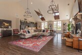 Located at 18101 Golden Bear Trace in Moseley, VA, this single-story clubhouse is designed to impress with its open-concept layout and soaring vaulted ceilings accented by rich wood beam detailing. The expansive main living area is anchored by a floor-to-ceiling stacked stone fireplace, complete with a mounted flat-screen television and generous hearth, creating a warm and inviting focal point. Rich hardwood flooring flows seamlessly throughout the entire space, complementing the neutral, light-filled interiors.

Walls of oversized windows bathe every corner of the space in natural light, offering views of the surrounding community and outdoor amenity areas, including what appears to be a pool and landscaped grounds. The vaulted ceiling features distinctive wood-clad skylights that further enhance the airy, open atmosphere.

The well-appointed kitchen area is outfitted with custom dark-stained cabinetry featuring sleek bar-pull hardware, granite countertops with under-cabinet lighting, and a stainless steel sink. A large central island with a stone countertop and bar seating provides ample space for gatherings and casual dining.

A secondary seating area with generous open floor space is ideal for flexible use, while a mini-split climate system ensures year-round comfort. Thoughtful equestrian-themed artwork ties in the character of the surrounding Golden Bear Trace community.