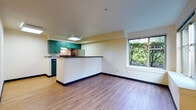 This single-floor unit offers a clean, functional layout designed for comfortable everyday living. The open-concept living and dining area flows seamlessly into the kitchen, which is defined by a peninsula-style breakfast bar with a dark countertop. The kitchen is equipped with teal-green cabinetry, a black electric range, a stainless steel refrigerator, and under-cabinet ventilation, all set above light hardwood-style flooring that extends throughout the unit. A large picture window in the living area frames lush, green outdoor foliage, filling the space with natural light and a connection to nature. The bedroom is a quiet, well-proportioned room with its own window overlooking greenery, a sliding closet, and direct access to a dedicated entry door with a keypad lock. Baseboard heating provides warmth throughout. The bathroom features a long vanity with a single sink, ample drawer storage, a wide mirror, and durable flooring that complements the rest of the unit. Dark blue baseboards provide a subtle contrast against the neutral, cream-toned walls throughout. The overall ambiance is bright, tidy, and move-in ready, with a practical design that maximizes the use of every area.