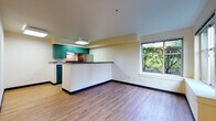 This single-floor unit offers a clean, functional layout designed for comfortable everyday living. The open-concept living and dining area flows seamlessly into the kitchen, which is defined by a peninsula-style breakfast bar with a dark countertop. The kitchen is equipped with teal-green cabinetry, a black electric range, a stainless steel refrigerator, and under-cabinet ventilation, all set above light hardwood-style flooring that extends throughout the unit. A large picture window in the living area frames lush, green outdoor foliage, filling the space with natural light and a connection to nature. The bedroom is a quiet, well-proportioned room with its own window overlooking greenery, a sliding closet, and direct access to a dedicated entry door with a keypad lock. Baseboard heating provides warmth throughout. The bathroom features a long vanity with a single sink, ample drawer storage, a wide mirror, and durable flooring that complements the rest of the unit. Dark blue baseboards provide a subtle contrast against the neutral, cream-toned walls throughout. The overall ambiance is bright, tidy, and move-in ready, with a practical design that maximizes the use of every area.