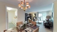 This well-appointed 2-bedroom, 2-bathroom residence offers a cohesive single-floor layout that balances comfort and style. The open-concept living and dining area serves as the heart of the home, where an elegant gold chandelier anchors the dining space, complemented by crown molding and warm neutral tones throughout. The living room features a classic fireplace flanked by dark wood display shelving, and a sliding glass door that floods the space with natural light while providing access to a private balcony with outdoor views. A dedicated accent wall in soft teal adds a refined pop of color to the living area. The galley-style kitchen is outfitted with white cabinetry, white appliances including a gas range, ample counter space, and a pass-through window that connects to the dining area. The primary bedroom is generously proportioned, featuring plush carpeting, warm accent walls, and direct access to both a walk-in closet with wire shelving and an en-suite bathroom with a glass-enclosed shower. The second bedroom is equally comfortable, with large windows and soft carpeting. A second full bathroom includes a tub-shower combination, a white vanity, and tile flooring. Crown molding and neutral tones carry throughout, creating a warm, inviting ambiance across the entire residence.