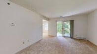 This single-floor residence offers a thoughtfully arranged layout with a clean, neutral aesthetic throughout. The living area is bright and open, featuring wall-to-wall carpeting and a sliding glass door that leads to a private balcony with a metal railing, framing lush tree views and allowing natural light to fill the space. An open passage connects the living area to an additional room, enhancing the sense of flow between spaces.

The kitchen is functional and well-appointed, featuring warm wood cabinetry with brushed metal hardware, dark laminate countertops, and light hardwood-style flooring. White appliances, including a refrigerator, electric range with built-in microwave, and dishwasher, are neatly integrated throughout.

The bedrooms are carpeted and generously proportioned, each offering ample natural light through blinds-fitted windows. One bedroom includes a walk-in closet with built-in shelving, while another features a dedicated closet with bifold doors. A separate dining or flex room provides additional versatility, accented by a multi-light chandelier.

The bathroom includes a wood-toned vanity with a white countertop, dual mirrors, and a full soaking tub with surrounding surround walls, completing this well-organized residence.