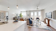 This thoughtfully designed single-floor residence offers a seamless blend of comfort and modern style throughout its open, airy layout. The heart of the home is the open-concept living and dining area, where wide-plank wood-look flooring, a ceiling fan, and an abundance of natural light from multiple windows create a warm and inviting atmosphere. French doors lead directly to a private balcony, extending the living space outdoors with pleasant surrounding views.

The kitchen is a functional centerpiece, featuring rich dark-stained cabinetry, light quartz countertops, stainless steel appliances, a subway tile backsplash, and a central island with seating for two — ideal for casual dining or entertaining. Pendant lighting adds a refined touch overhead.

The dining area sits adjacent to the living space, bathed in natural light from large windows dressed with classic plantation shutters and sheer curtains. The bedrooms offer plush carpeting and generous windows that invite natural light, while the primary suite includes access to a walk-in closet with multi-level shelving and hanging rods. The bathrooms are clean and well-appointed, with one featuring a tiled walk-in shower and another with a full soaking tub and shower combo, both complemented by wood-toned vanities and crisp white finishes throughout.