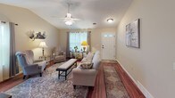 This single-story home offers a thoughtfully designed layout with a welcoming ambiance throughout. The living room serves as the heart of the home, featuring vaulted ceilings with a ceiling fan, rich hardwood flooring, and a front entry door with glass panel accents that invite natural light. The space flows into a versatile sitting area with additional vaulted ceilings, a large window with sheer curtains, and a decorative wall shelf — ideal for relaxed reading or quiet conversation.

The kitchen is equipped with dark wood cabinetry, granite-style countertops, a gas range, and an over-the-range microwave. A window above the counter frames a pleasant outdoor view, adding a bright, airy feel to the cooking space. Adjacent to the kitchen, a dining area features a decorative stained-glass entry door that adds a charming architectural detail.

The bedrooms are carpeted and comfortably sized, each with closet access and natural light from well-placed windows. The bathroom presents dark wood vanity cabinetry with a granite-style countertop, a full shower, and wood-look flooring. A dedicated laundry area with side-by-side washer and dryer adds everyday convenience. A flexible bonus room with hardwood floors provides additional living or hobby space, completing this warm and functional home.