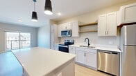 This well-appointed one-bedroom, one-bathroom residence in Hastings, MN offers a thoughtfully designed layout that maximizes both comfort and functionality. The open-concept kitchen and living area serves as the heart of the home, showcasing white shaker cabinetry, white quartz countertops, a central island with pendant lighting, and a full suite of stainless steel appliances including a range, microwave, dishwasher, and refrigerator. Light wood-style flooring runs throughout the main living areas, lending a clean and contemporary feel. The living room opens directly to a private balcony through sliding glass doors, bringing in abundant natural light and outdoor views. The bedroom is carpeted for warmth and comfort, featuring a window with exterior views, a closet, and direct access to the in-unit laundry area, which is equipped with a full-size washer and dryer. The bathroom is finished with light wood-look flooring, a white vanity with matte black hardware, and a full tub-shower combination. Neutral warm-toned walls, matte black hardware accents, and consistent modern detailing tie the entire space together into a cohesive and inviting living environment.