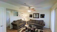 This two-story home offers a thoughtfully arranged layout that balances functionality and comfort. The main living area serves as the heart of the space, featuring hardwood flooring, a textured ceiling, and a ceiling fan with integrated lighting that provides both airflow and ambient illumination. Crown molding adds a refined architectural detail along the upper edges of the walls, contributing to a polished, well-finished interior.

Built-in wall shelving provides practical display and storage space, adding character to the living room. The open, airy feel of the room is enhanced by its generous proportions, allowing for a comfortable seating arrangement. A staircase visible from the living area connects the two floors, reinforcing the home's multi-level layout.

The neutral color palette throughout the living space creates a versatile backdrop, lending itself well to a variety of interior styles. Wall-mounted decorative accents and a centrally positioned mirror add visual interest and depth to the room. Overall, the space presents a warm and inviting atmosphere, with practical features and classic design elements that make it well-suited for everyday living and entertaining alike.
