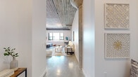 Located in Alameda, CA, this one-bedroom, one-bathroom loft showcases a striking industrial-modern aesthetic defined by soaring exposed concrete ceilings with visible structural beams and pipes, polished concrete floors, and original concrete columns that speak to the building's architectural heritage. The open-concept main living area flows seamlessly from the living room to the dining space and kitchen, creating a bright, cohesive environment. Large windows usher in generous natural light, enhancing the airy feel of the space. The kitchen features warm wood cabinetry, a subway tile backsplash, stainless steel appliances, and ample counter space. The living and dining areas offer a generous, flexible layout ideal for both relaxing and entertaining. The bedroom is a serene retreat with wide windows that frame exterior views and light wood flooring, providing a warm contrast to the industrial elements found throughout. The bathroom is clean and modern, finished with large-format tile flooring, subway tile surrounding a full soaking tub and shower, and crisp white fixtures. Throughout the loft, the interplay of raw industrial materials and refined modern finishes creates a compelling, urban ambiance that is both functional and visually distinctive.